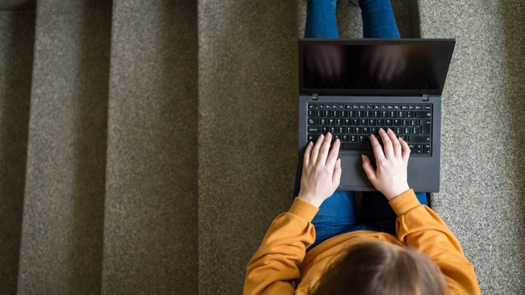 A girl is sitting on the stairs with her laptop.