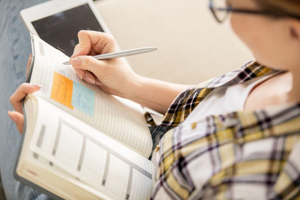 A woman writing in a notebook while holding an ipad.