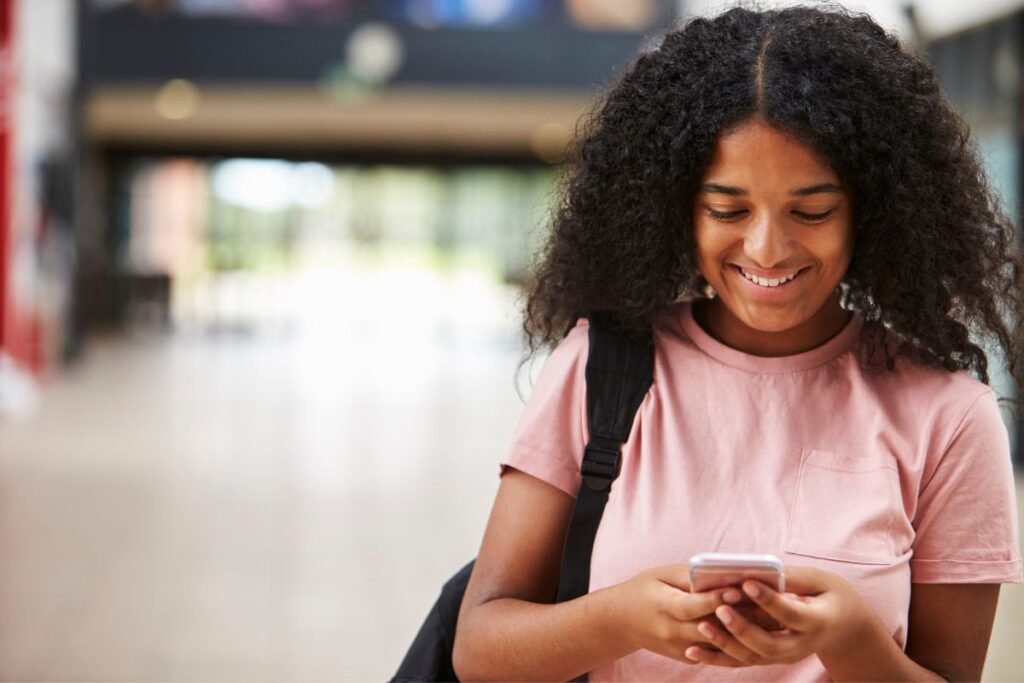 A young black girl is using her cell phone in a school hallway.