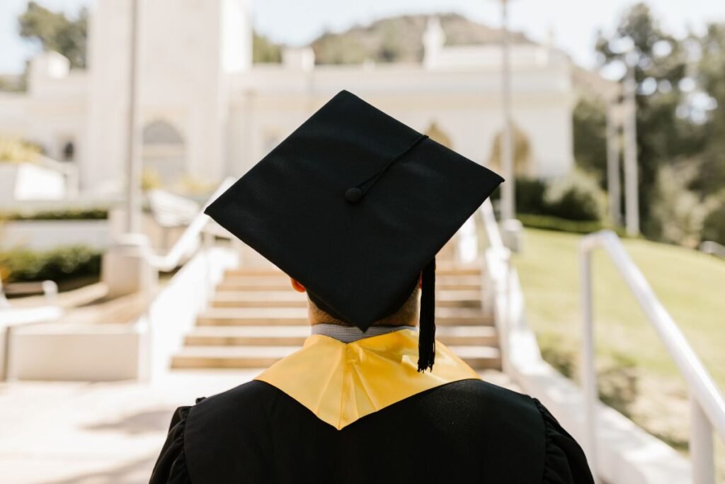 Graduate in cap and gown facing a building with steps.