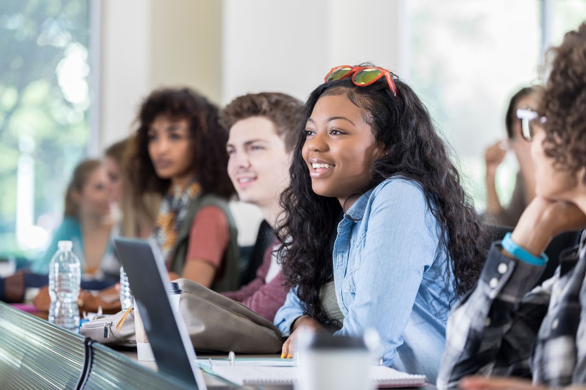 In a classroom setting, students sit at desks with laptops and notebooks, attentively exploring the difference between college and university.