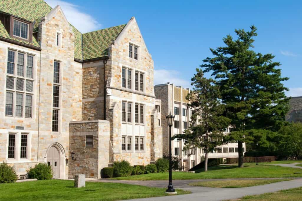 A stone academic building with large windows and a green lawn sits beside a tall tree under a clear blue sky—it’s the perfect spot for students to review common medical school interview questions before their big day.