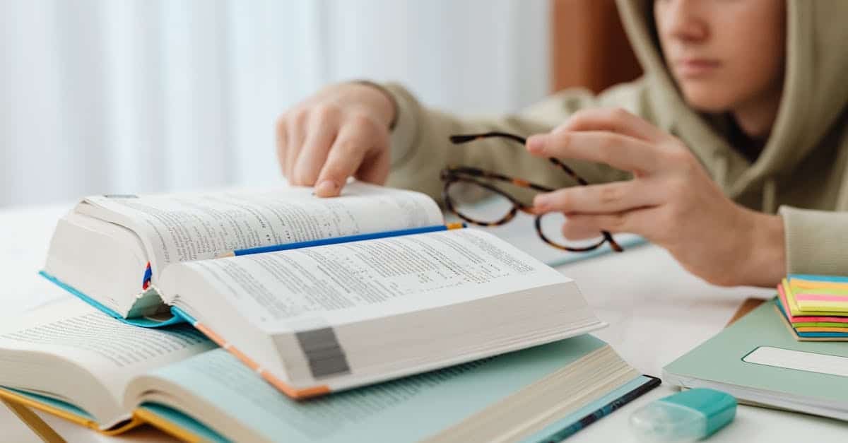 Focused teenager studying with open textbooks, eyeglasses, and notes.